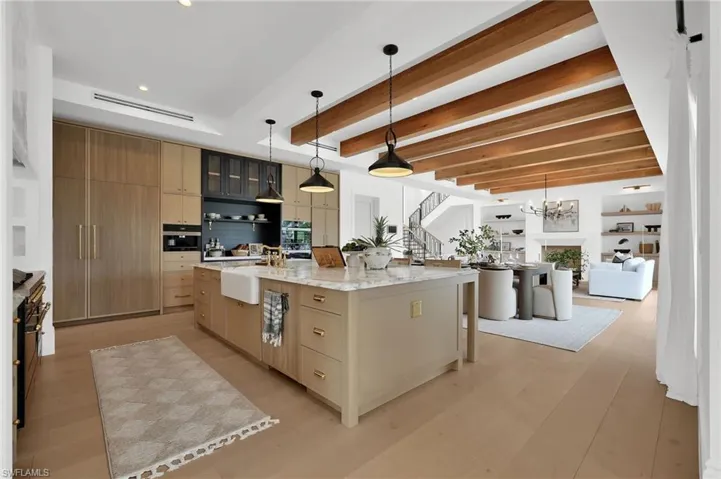 Kitchen with pendant lighting, modern cabinets, a kitchen bar, light stone counters, and beamed ceiling