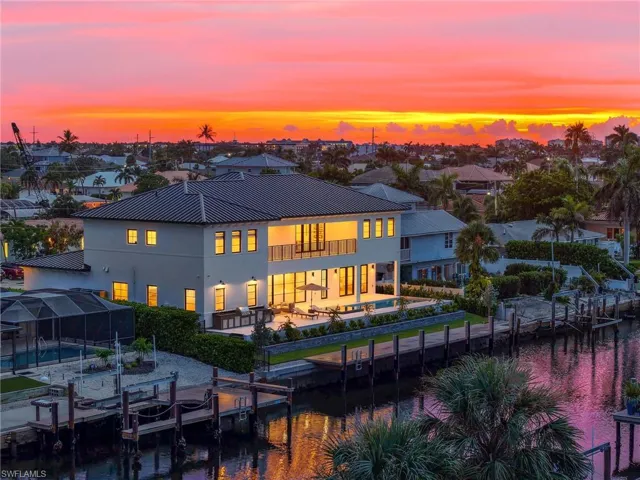 Back of property at dusk featuring an outdoor pool, a patio, stucco siding, a balcony, and a metal roof