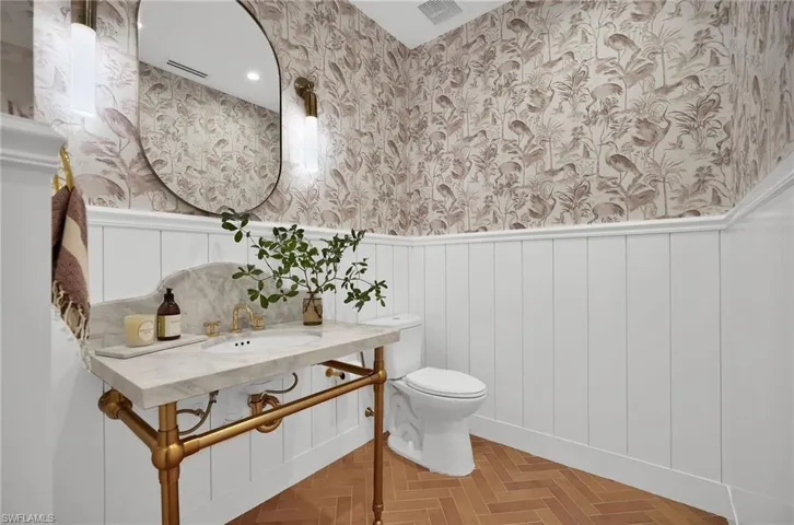 Half bathroom with wallpapered walls, wainscoting, and a decorative wall