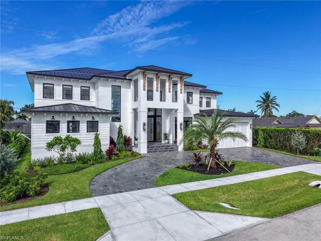 Drone view of the front of this Marco Island luxury home showcasing the grand façade, metal roof, circular driveway, and lush landscaping.
