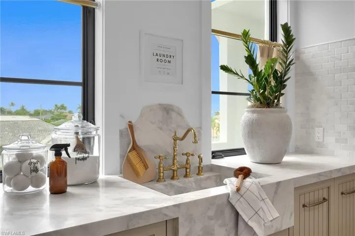 Spacious laundry with limestone checkerflooring, custom cabinetry, and a deep sink fitted with Brizo fixtures. Designed for both function and style, it offers ample workspace and storage.