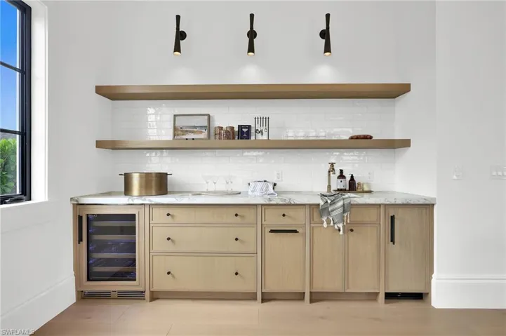 Custom white oak cabinetry with open shelving, Broderick collection fixtures, wine fridge, and ice maker designed for effortless entertaining.