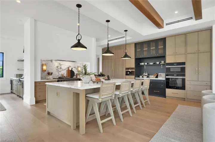 Kitchen with open shelves, hanging light fixtures, glass insert cabinets, light stone countertops, and a kitchen breakfast bar
