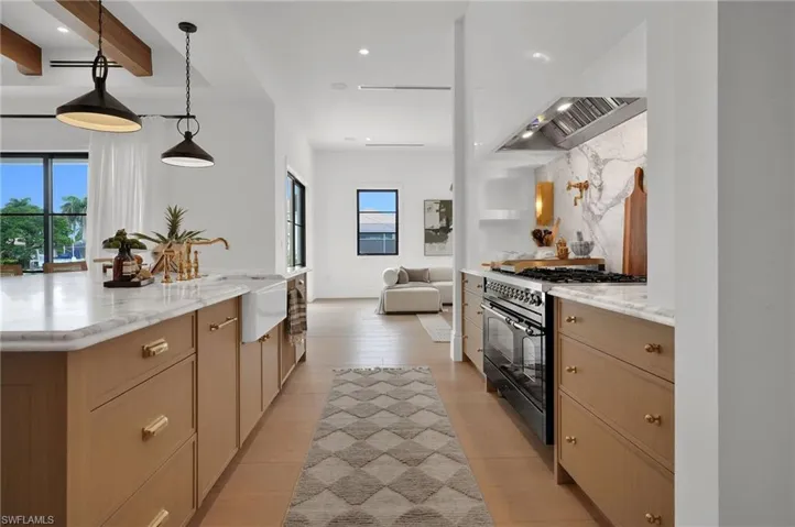 Kitchen featuring light stone countertops, decorative light fixtures, range with two ovens, recessed lighting, and a large island with sink