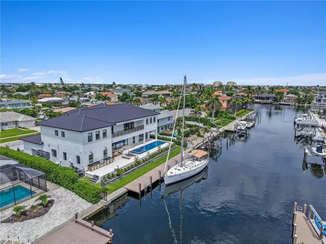 High-altitude daytime drone view of Marco Island luxury waterfront estate with saltwater pool, 53-ft docked sailboat, and wide views of the surrounding town and waterways.