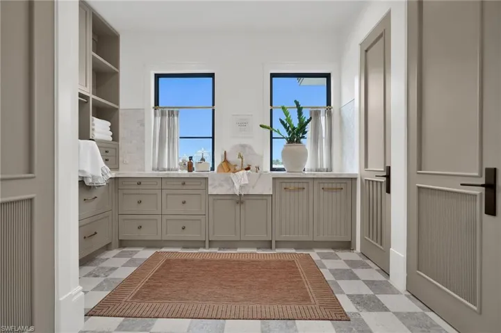 Spacious laundry equipped with LG ThinQ double washer and dryer, marble countertops, checkered flooring, and deep sink with Brizo fixtures.