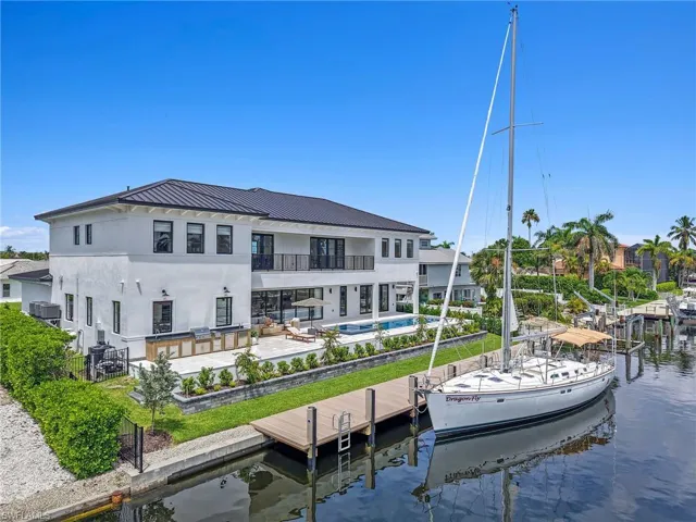 Back of property Daytime drone view of Marco Island luxury waterfront home with saltwater pool, spacious backyard, and a 53-ft sailboat docked at the private deep-water dock. pool, a water view, and a patio area