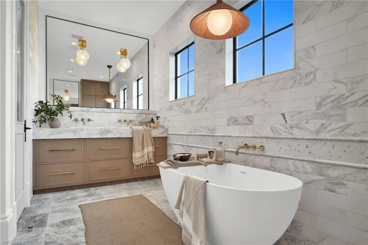 Bathroom with tile walls, a freestanding bath, double vanity, and decorative backsplash