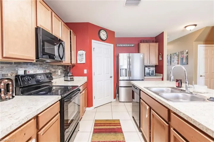 Kitchen with sink, black appliances, tasteful backsplash, and light tile floors