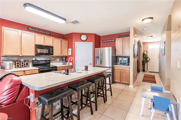 Kitchen featuring sink, a breakfast bar, tasteful backsplash, and black appliances