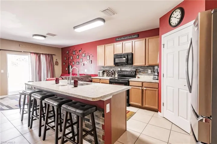 Kitchen featuring a center island with sink, black appliances, light tile flooring, and a breakfast bar
