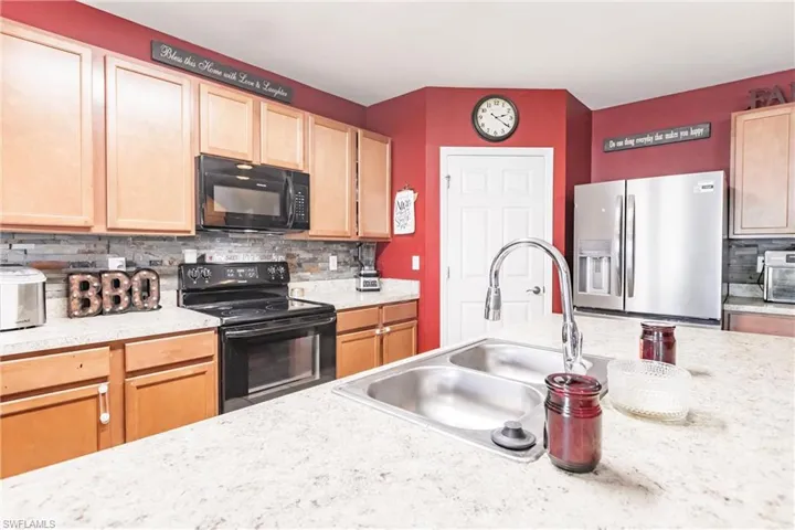 Kitchen with light stone countertops, sink, backsplash, and black appliances