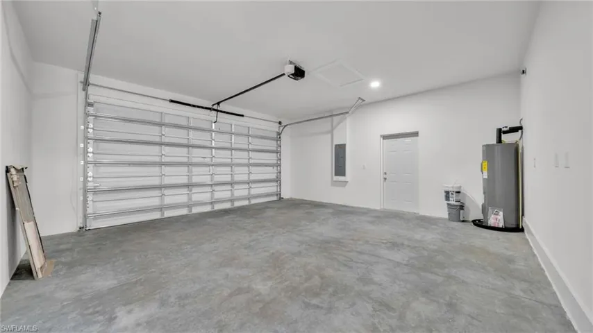 Garage with electric water heater, electric panel, and a garage door opener