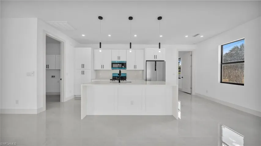 Kitchen featuring hanging light fixtures, stainless steel fridge, an island with sink, recessed lighting, and white cabinetry