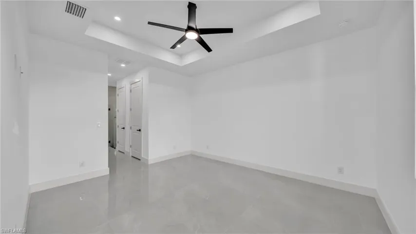Empty room with a raised ceiling, a ceiling fan, recessed lighting, and concrete floors