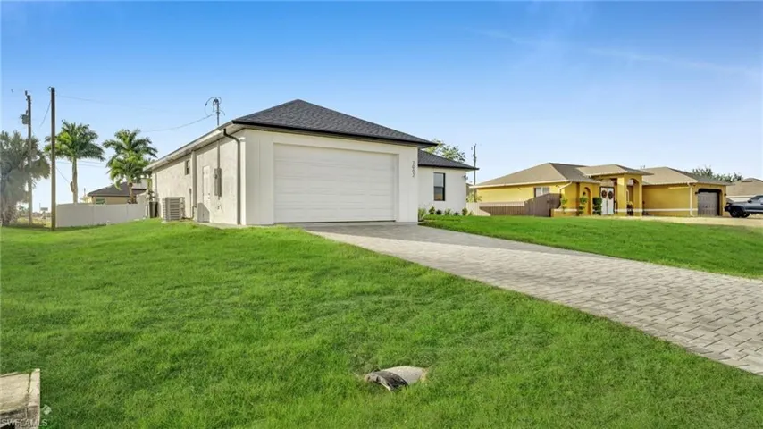 View of side of property featuring decorative driveway, stucco siding, a shingled roof, and a garage
