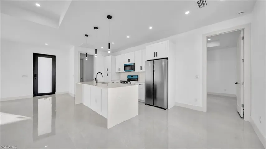 Kitchen with freestanding refrigerator, white cabinets, pendant lighting, a kitchen island with sink, and electric range