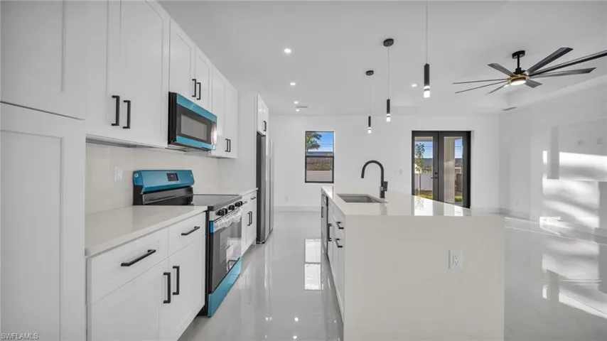 Kitchen with appliances with stainless steel finishes, white cabinetry, recessed lighting, decorative light fixtures, and light stone countertops