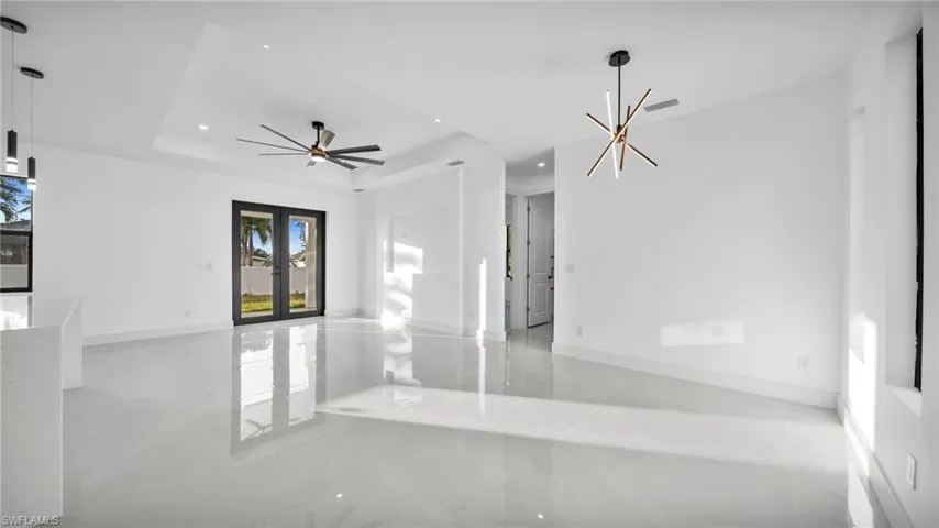 Empty room with a tray ceiling, light marble finish flooring, a chandelier, recessed lighting, and french doors