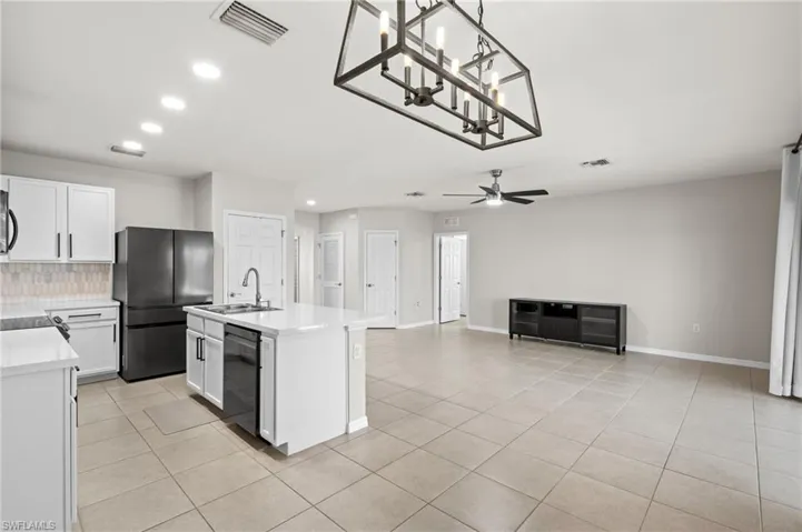 Kitchen with sink, white cabinets, a kitchen island with sink, light tile patterned floors, and black appliances