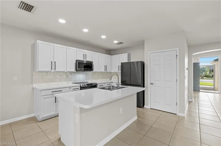 Kitchen with light tile patterned flooring, sink, a center island with sink, stainless steel appliances, and white cabinets