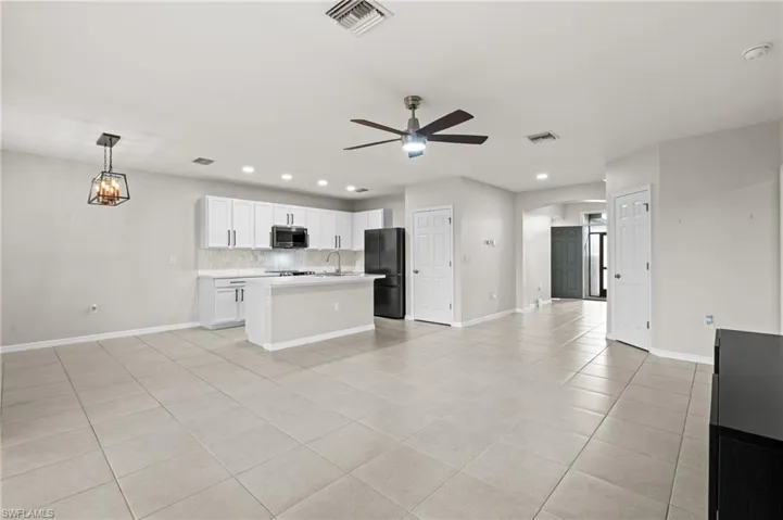 Kitchen featuring ceiling fan with notable chandelier, decorative light fixtures, tasteful backsplash, white cabinetry, and black fridge