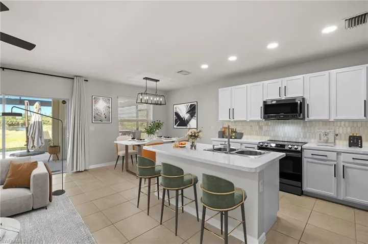 Kitchen featuring electric stove, white cabinetry, hanging light fixtures, a kitchen breakfast bar, and an island with sink