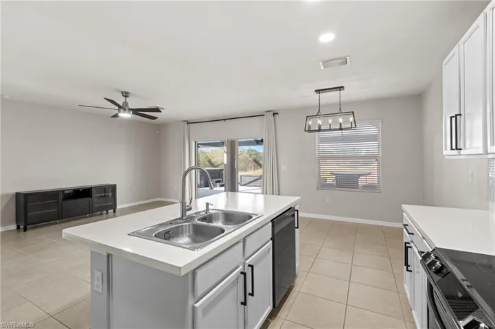Kitchen featuring range with electric stovetop, black dishwasher, sink, hanging light fixtures, and a kitchen island with sink