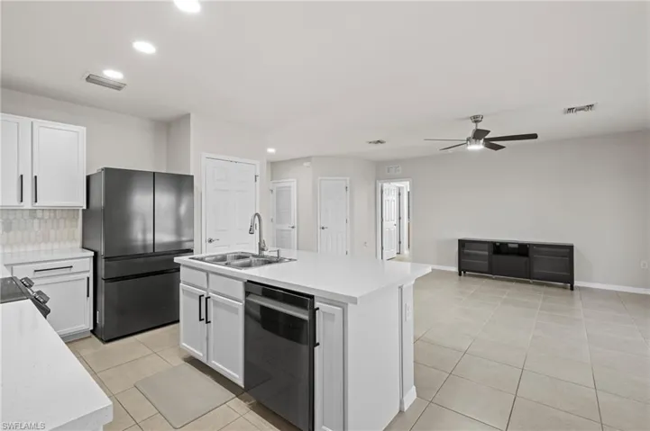 Kitchen featuring sink, white cabinetry, fridge, black dishwasher, and an island with sink