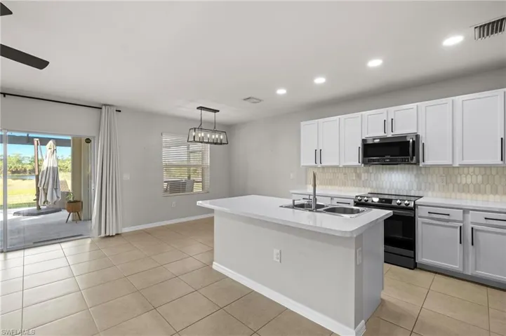 Kitchen with stainless steel appliances, white cabinetry, a center island with sink, and light tile patterned flooring