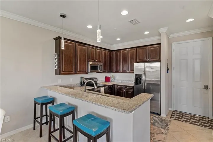 Kitchen with light stone countertops, appliances with stainless steel finishes, kitchen peninsula, light tile patterned floors, and decorative light fixtures