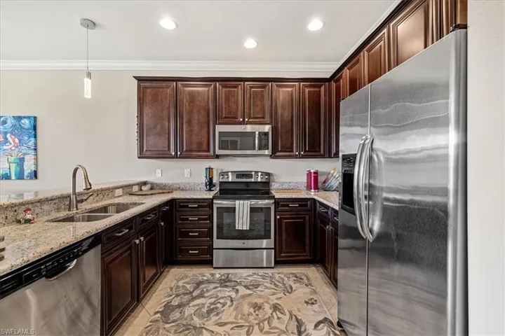Kitchen featuring light stone counters, dark brown cabinets, stainless steel appliances, sink, and decorative light fixtures