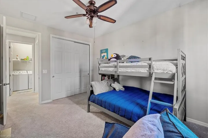 Carpeted bedroom featuring ceiling fan, independent washer and dryer, and a closet
