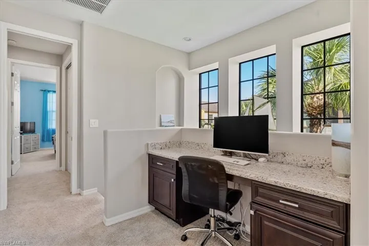 Home office featuring plenty of natural light, built in desk, and light carpet