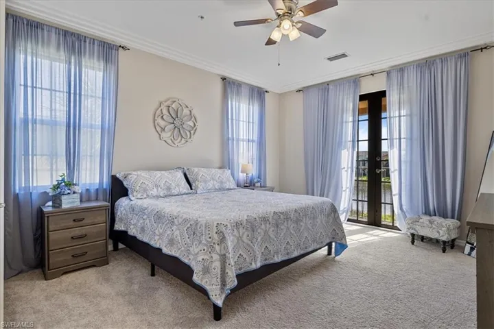 Carpeted bedroom with multiple windows, ceiling fan, french doors, and ornamental molding