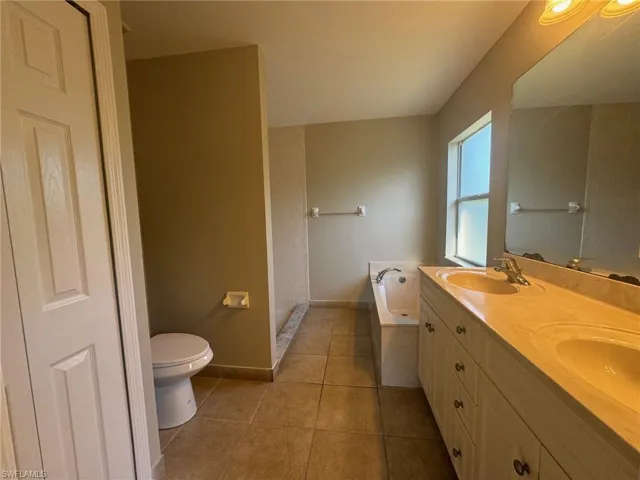 Bathroom with a tub, double vanity, tile flooring, and toilet