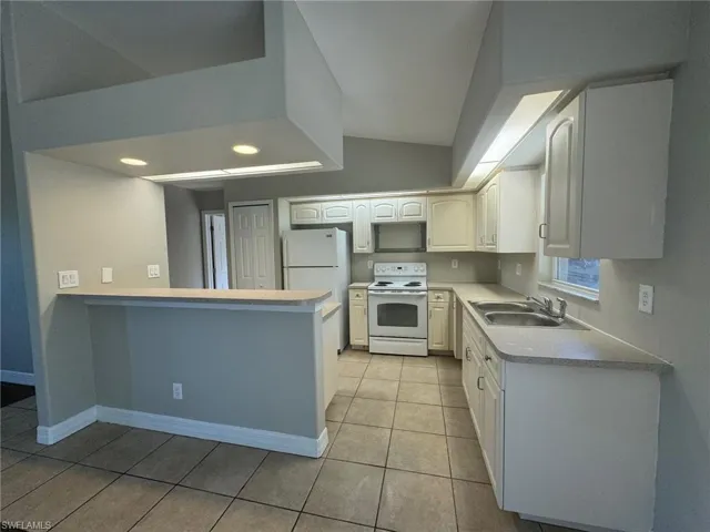 Kitchen with kitchen peninsula, white appliances, light tile floors, sink, and white cabinetry