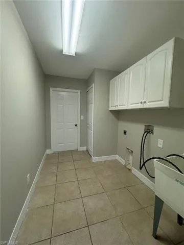 Washroom featuring electric dryer hookup, cabinets, light tile floors, and hookup for a washing machine