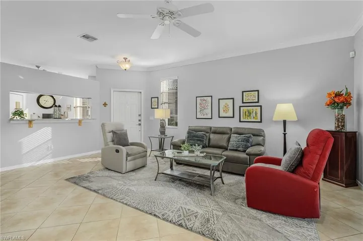 Living area with a ceiling fan, visible vents, baseboards, tile patterned flooring, and crown molding