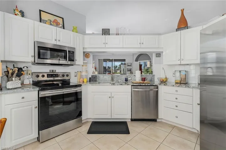 Kitchen with light tile patterned floors, stainless steel appliances, decorative backsplash, and white cabinetry