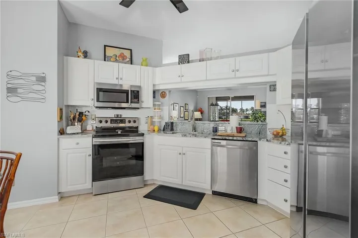 Kitchen featuring light stone countertops, stainless steel appliances, light tile patterned flooring, white cabinetry, and a sink