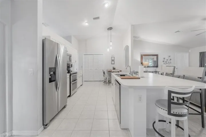 Kitchen with lofted ceiling, light tile patterned floors, appliances with stainless steel finishes, decorative light fixtures, and sink
