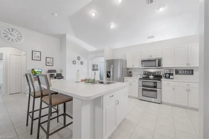 Kitchen featuring light tile patterned flooring, white cabinetry, a center island, appliances with stainless steel finishes, and vaulted ceiling