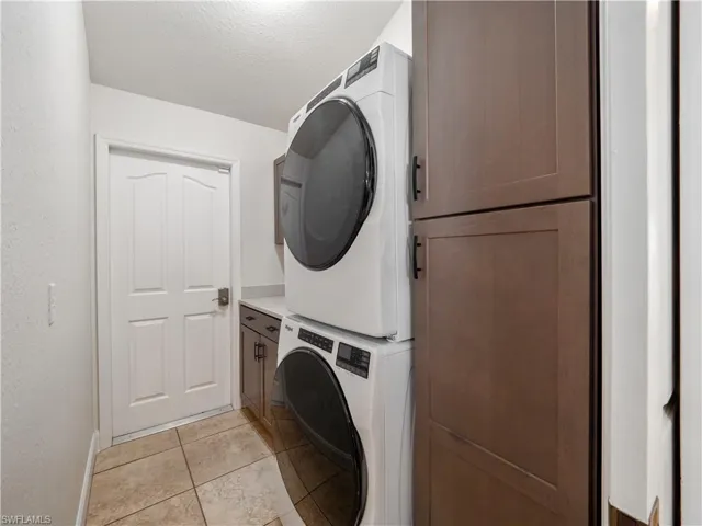 Laundry room featuring a textured ceiling, stacked washer and dryer, cabinets, and light tile patterned flooring