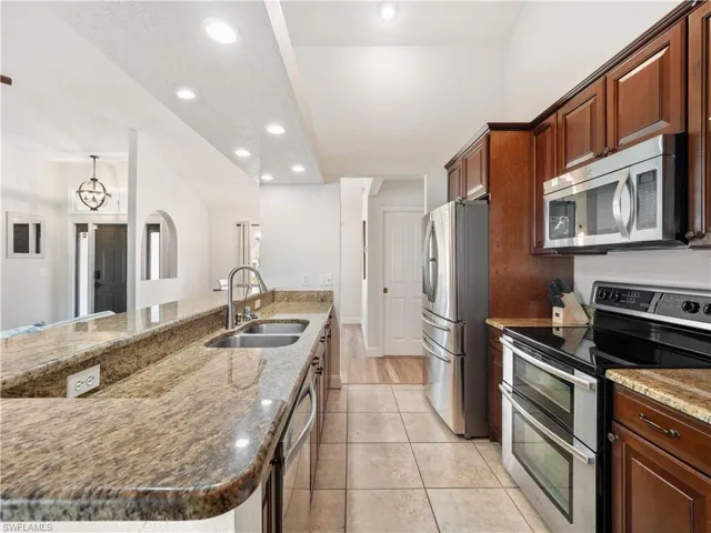 Kitchen with sink, light stone counters, appliances with stainless steel finishes, an inviting chandelier, and light hardwood / wood-style flooring