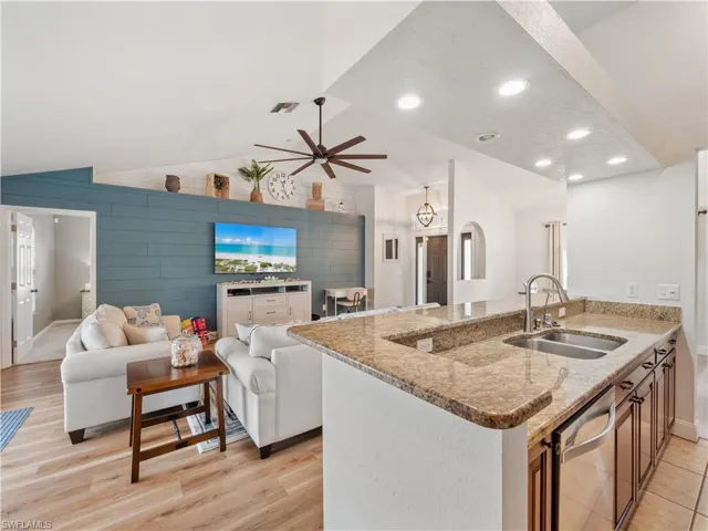 Kitchen with wood walls, light stone countertops, sink, light hardwood / wood-style floors, and lofted ceiling