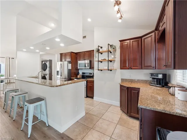 Kitchen featuring stacked washer / dryer, light stone counters, stainless steel appliances, plenty of natural light, and vaulted ceiling