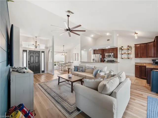 Living room featuring light hardwood / wood-style floors, ceiling fan with notable chandelier, and high vaulted ceiling