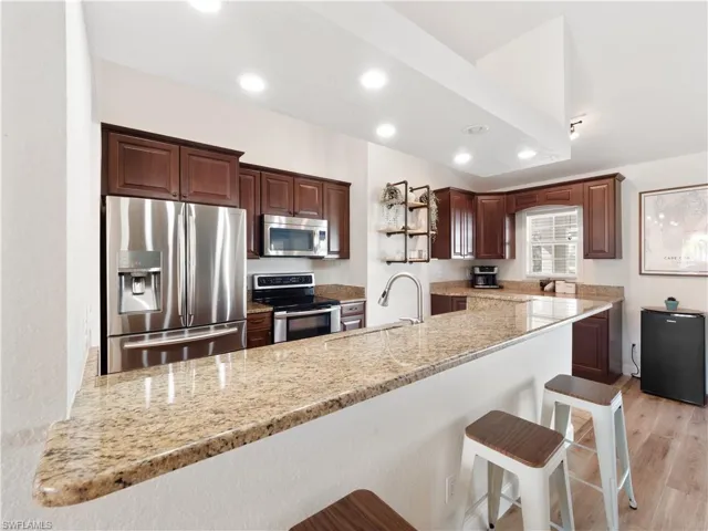 Kitchen with a kitchen bar, stainless steel appliances, kitchen peninsula, light stone countertops, and light hardwood / wood-style flooring