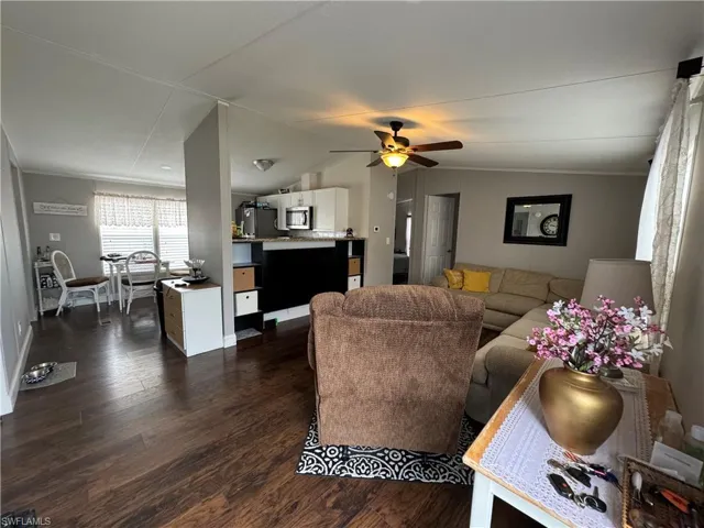 Living room with ceiling fan, vaulted ceiling, and dark wood-type flooring